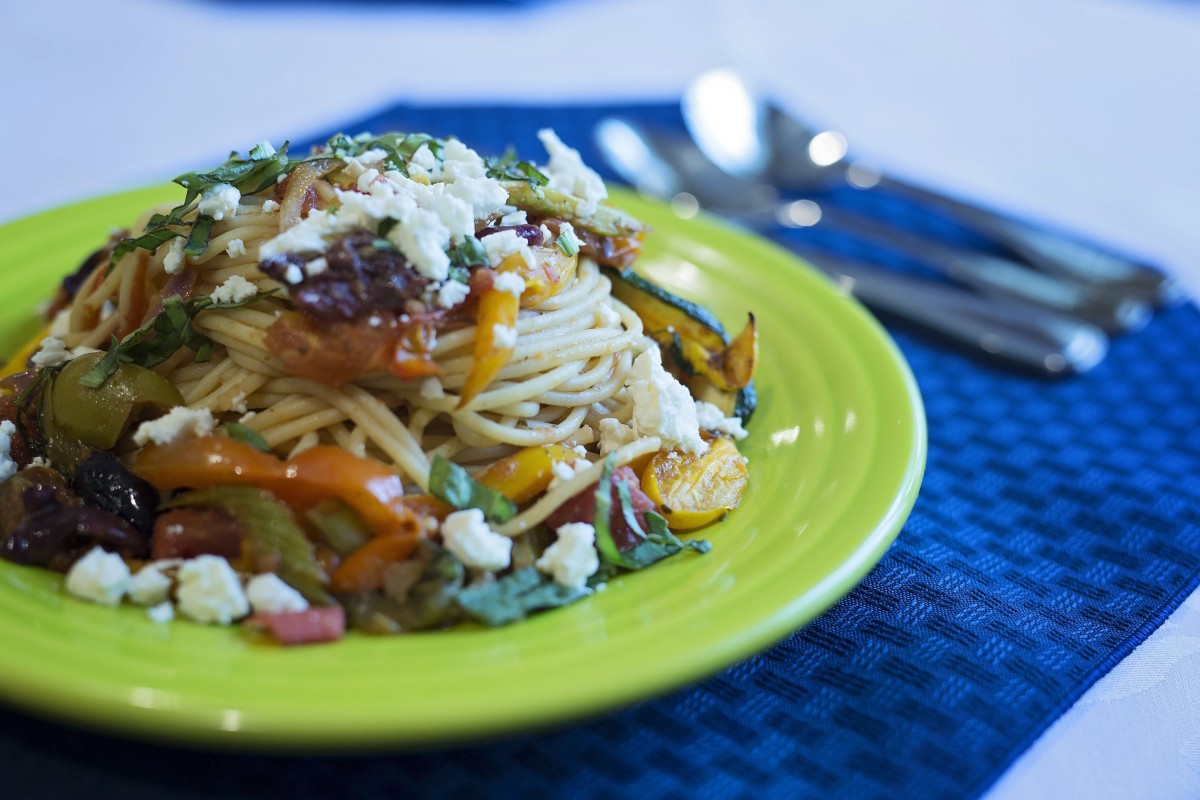 A vibrant plate of pasta with vegetables and cheese, served on a green dish.