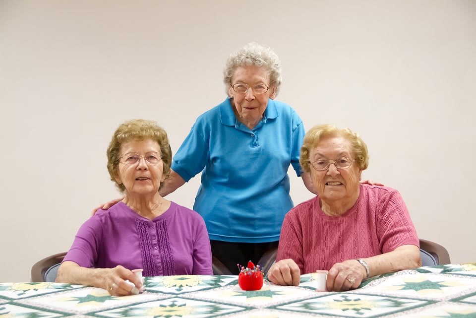 Three elderly women smiling and gathered around a table.