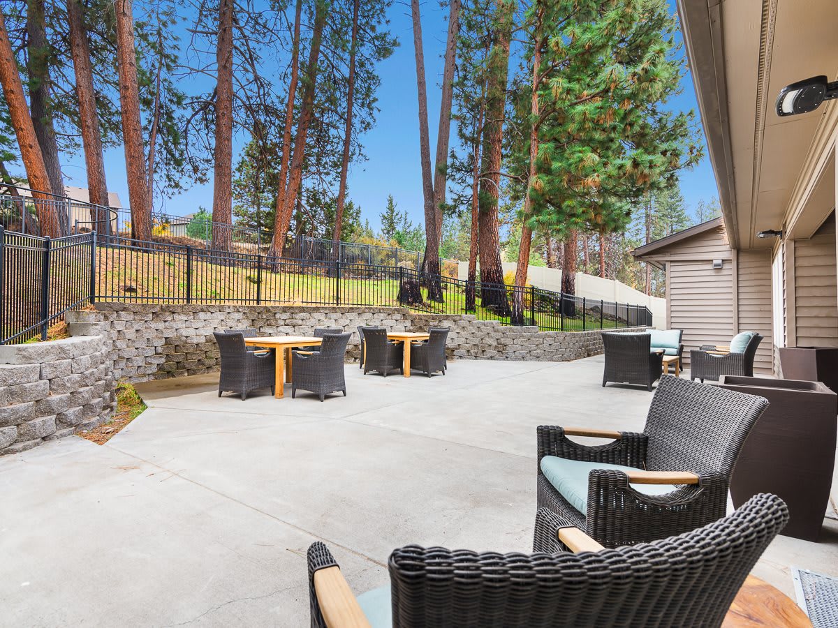 A spacious outdoor patio with wicker furniture, surrounded by tall trees.