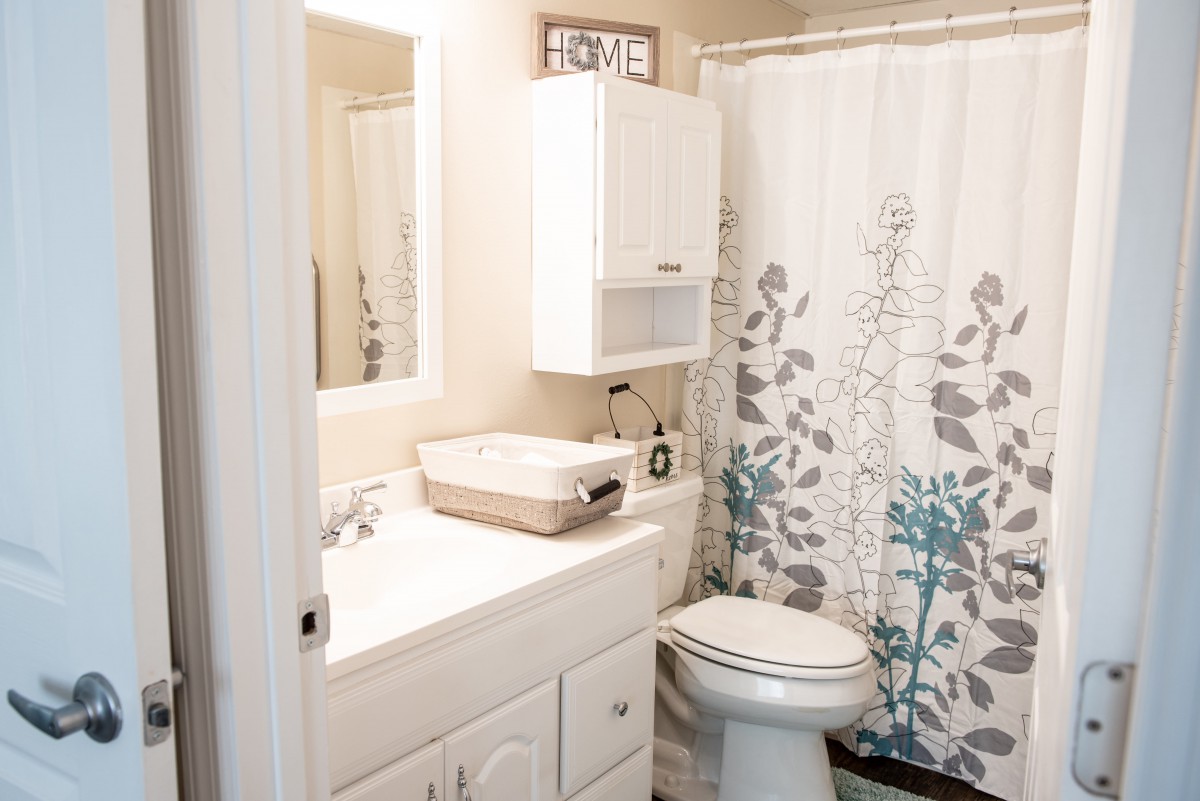 A neatly organized bathroom with a white sink, toilet, and floral shower curtain.