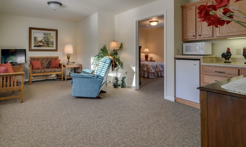 A cozy living room with a recliner chair, plants, and a view into the bedroom.