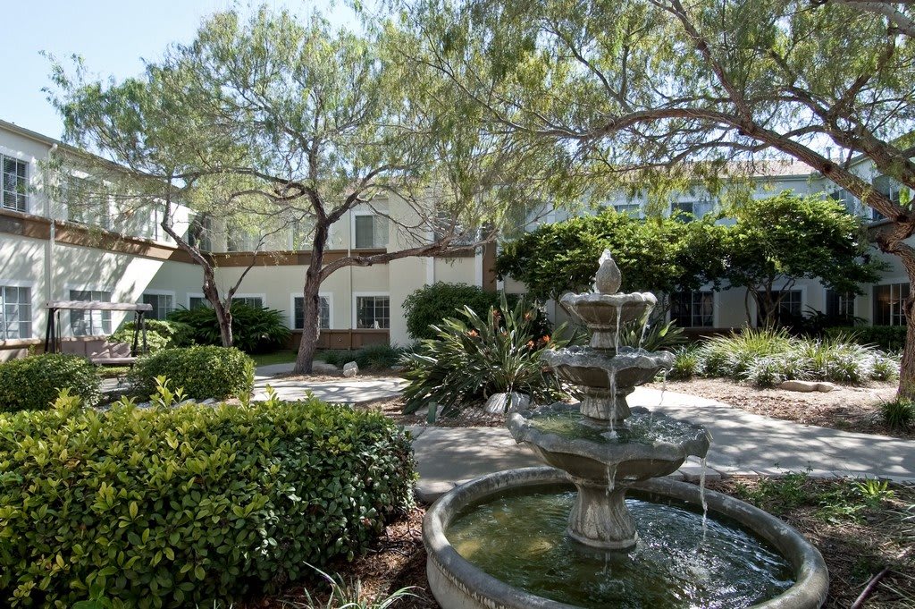 A serene garden with a fountain surrounded by lush greenery and buildings.