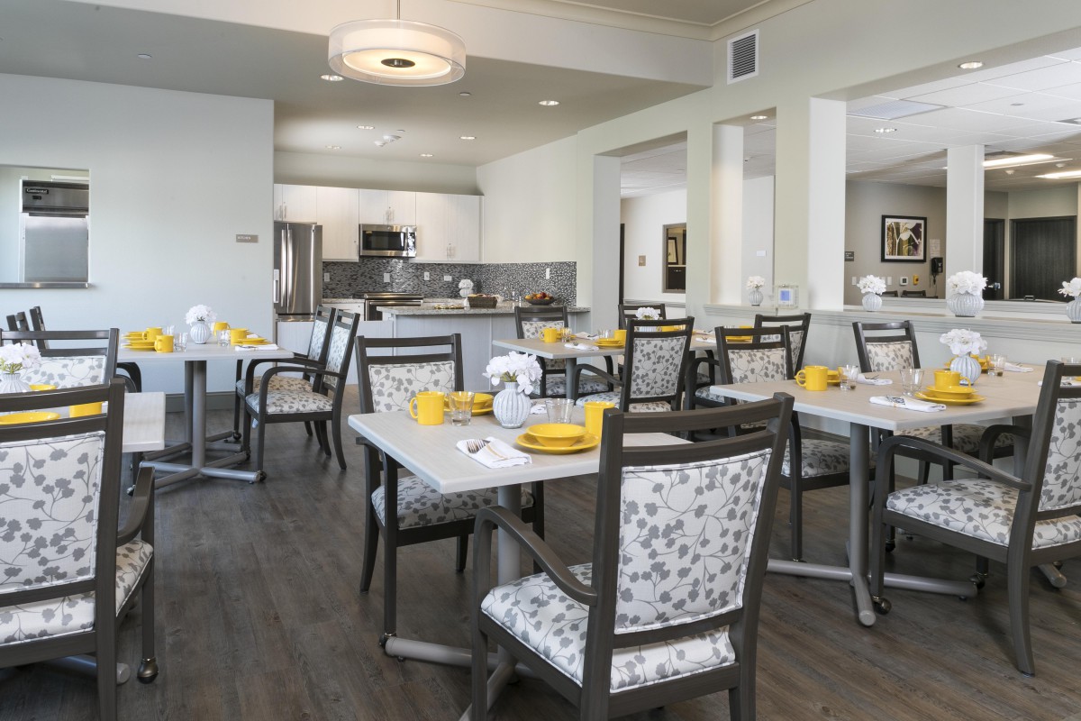 A modern dining room with elegantly set tables and a view of the kitchen area.