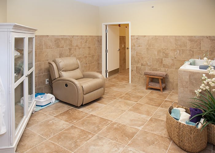 A cozy room featuring a recliner chair and tiled flooring, with a basket and shelf for storage.