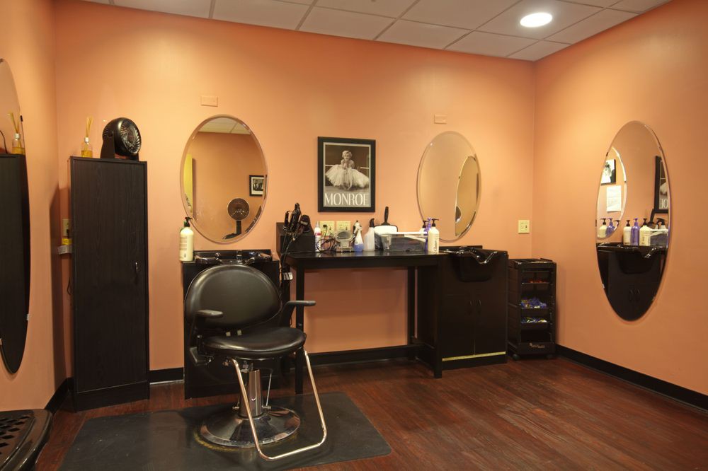 A cozy hair salon interior featuring a styling chair, mirrors, and salon equipment against orange walls.