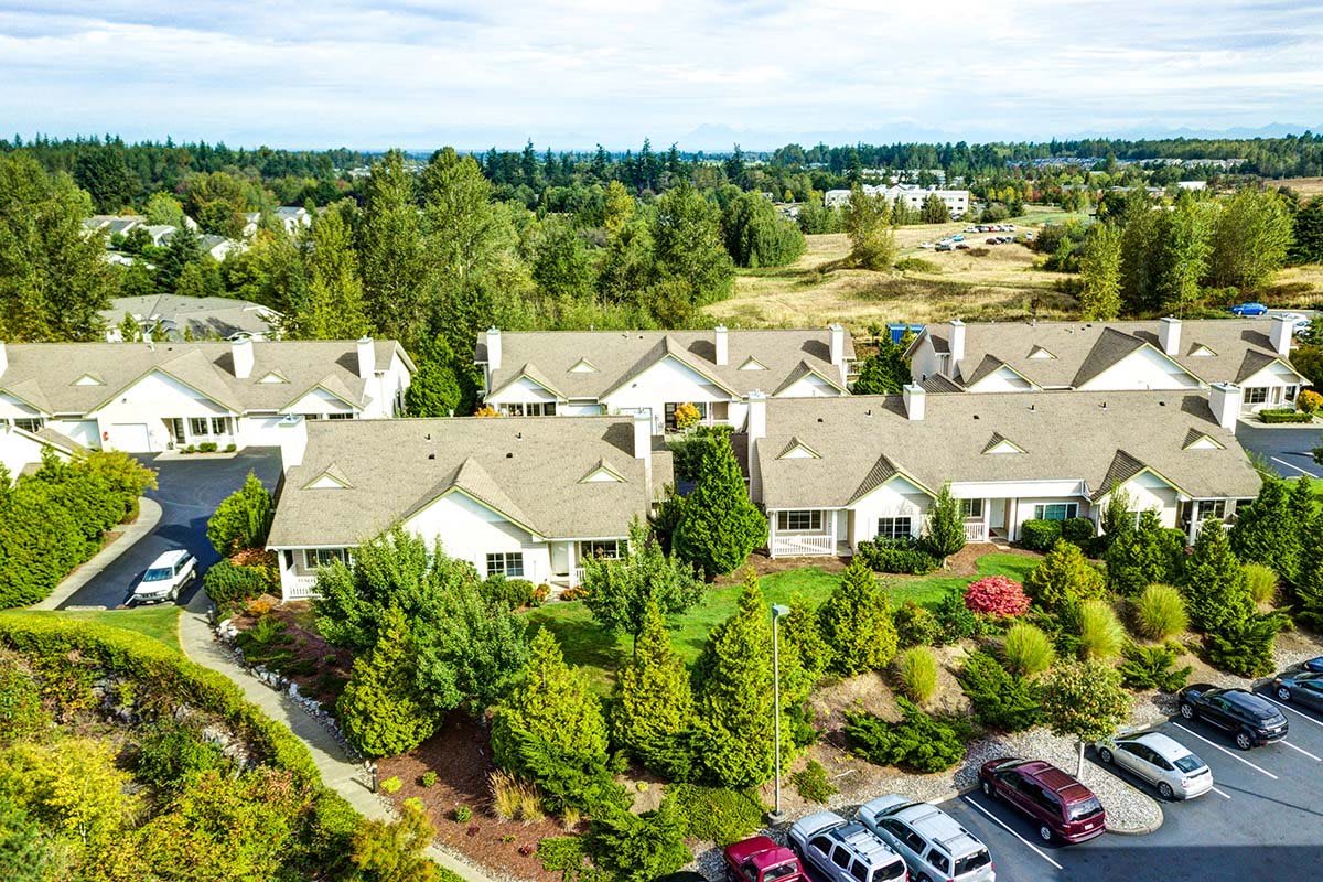 Aerial view of a suburban residential area with houses surrounded by greenery and a parking lot.