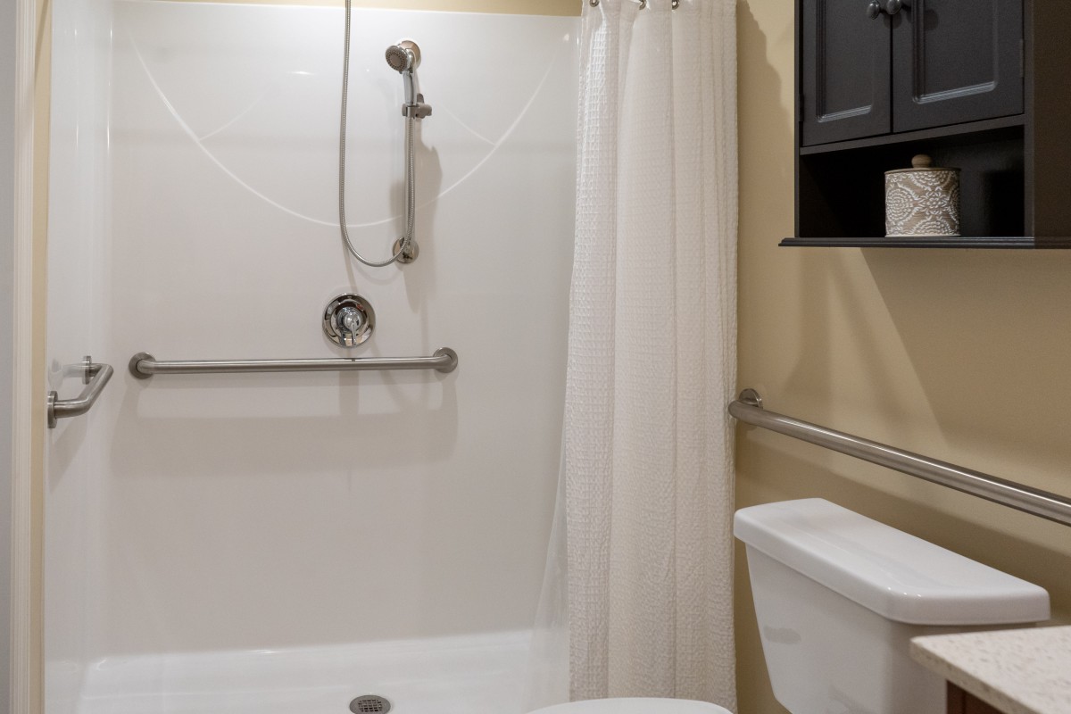 A bathroom with a bathtub, shower setup, and safety grab bars.