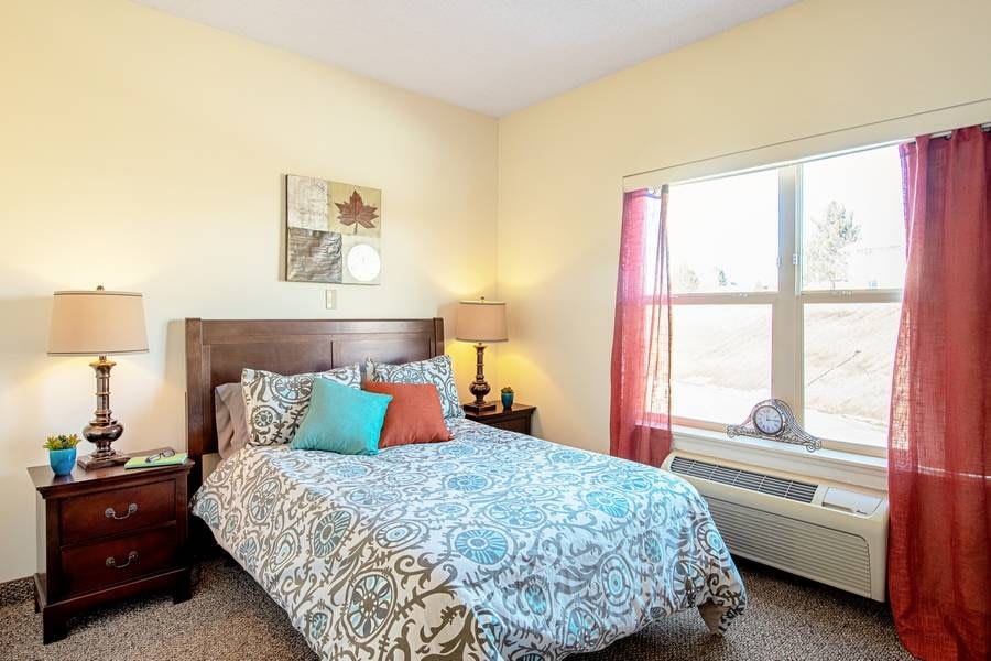 A cozy bedroom with a neatly made bed and colorful pillows, featuring a window allowing natural light to brighten the space.