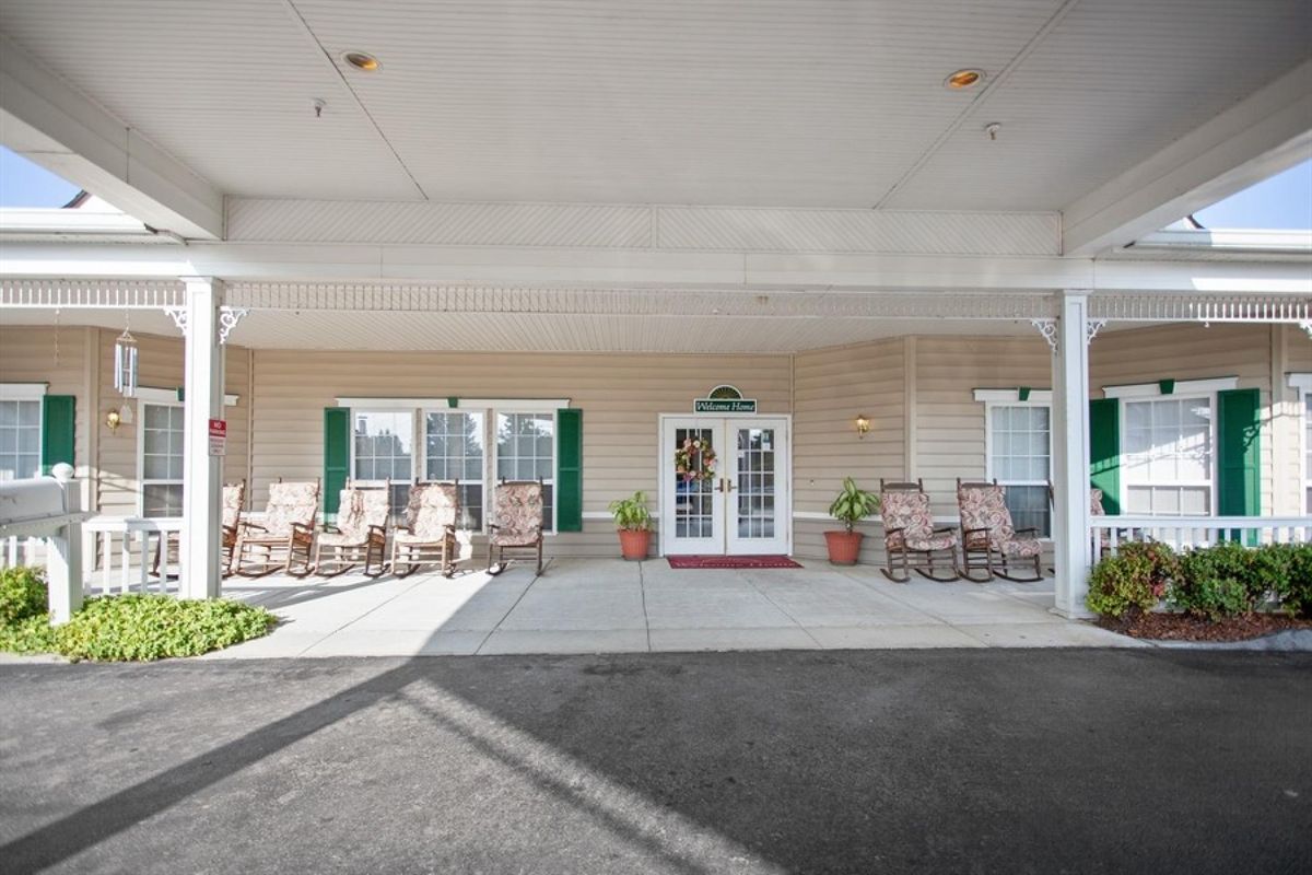 A covered entrance area with chairs and potted plants outside a building.