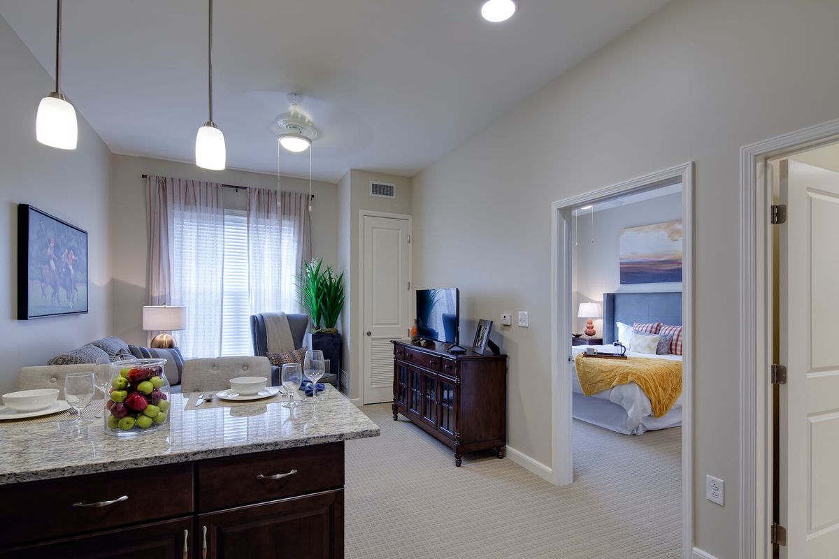 A modern apartment with an open-plan living room and kitchen, featuring a view into a cozy bedroom.
