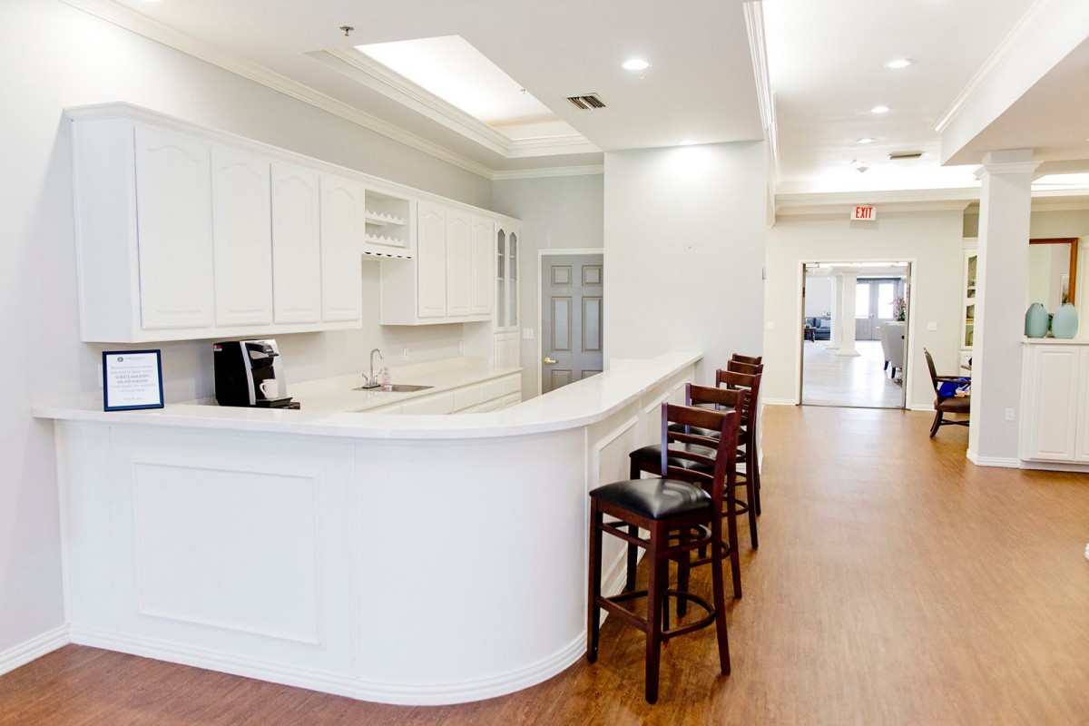 A modern kitchen interior featuring a white counter with bar stools, white cabinets, and wooden flooring.