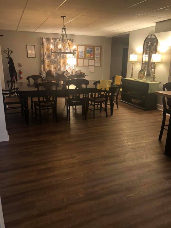 A cozy dining room with a wooden floor, featuring a large table surrounded by chairs, decorative lamps, and a chandelier.
