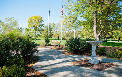 A serene park pathway lined with trees, featuring a bench and a birdbath.