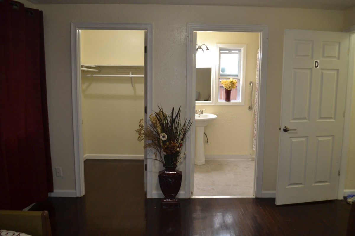 A view of a hallway leading to a walk-in closet and a bathroom, with a decorative vase in the foreground.