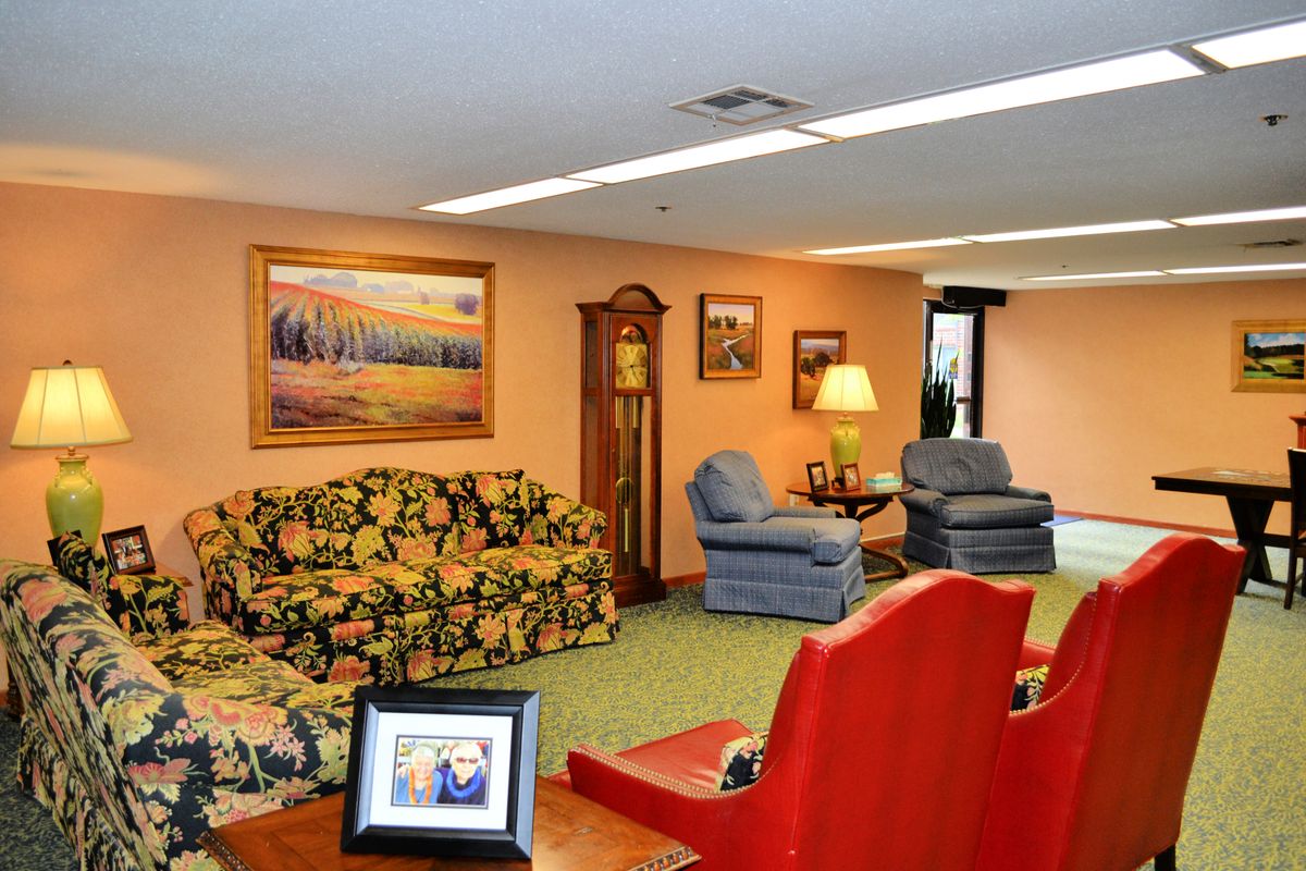 A cozy living room with floral sofa, blue armchairs, a grandfather clock, and decorative paintings.
