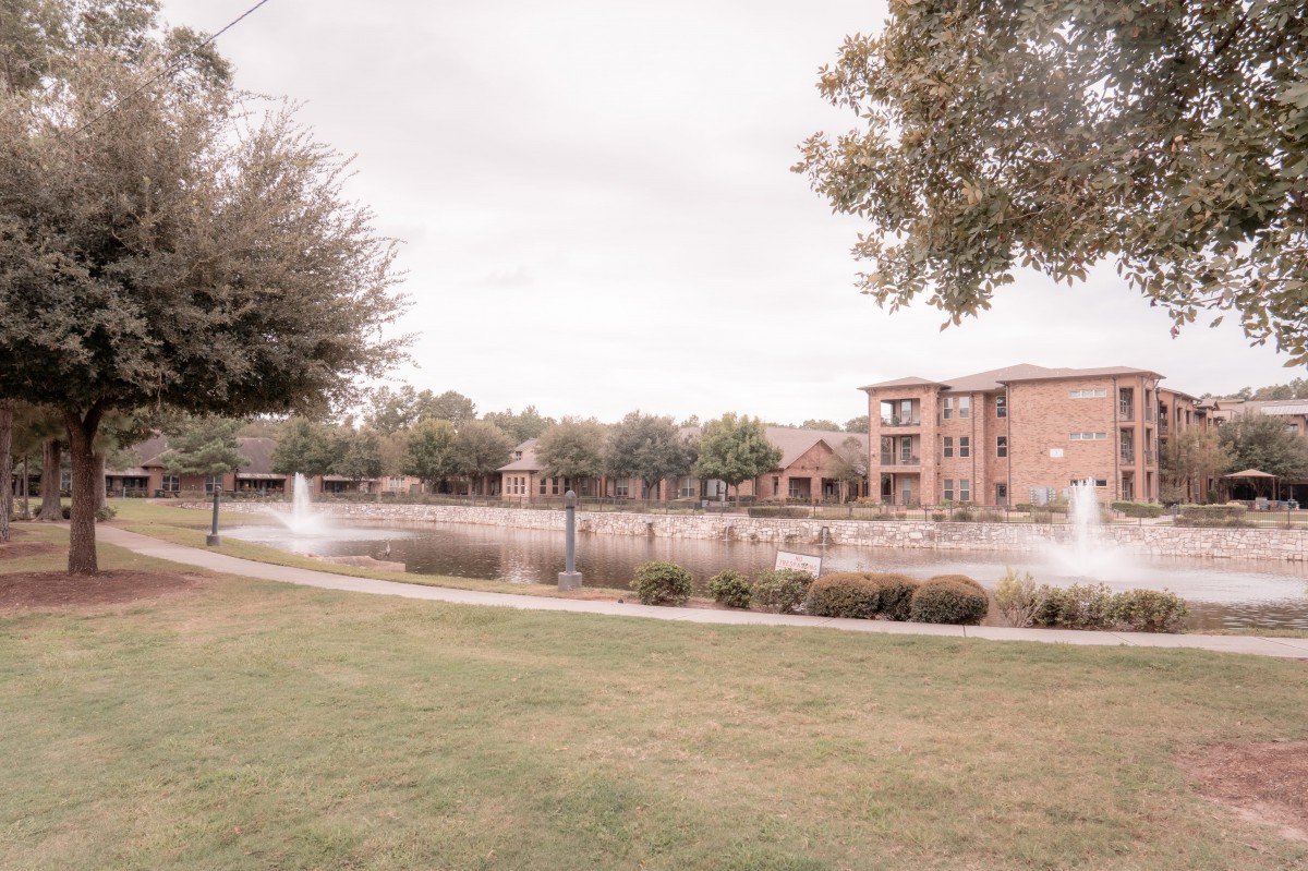 A serene landscape featuring a pond with fountains and an apartment building in the background.