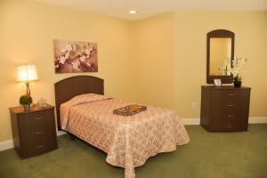 A cozy bedroom with a single bed, bedside table, and a dresser with a mirror.