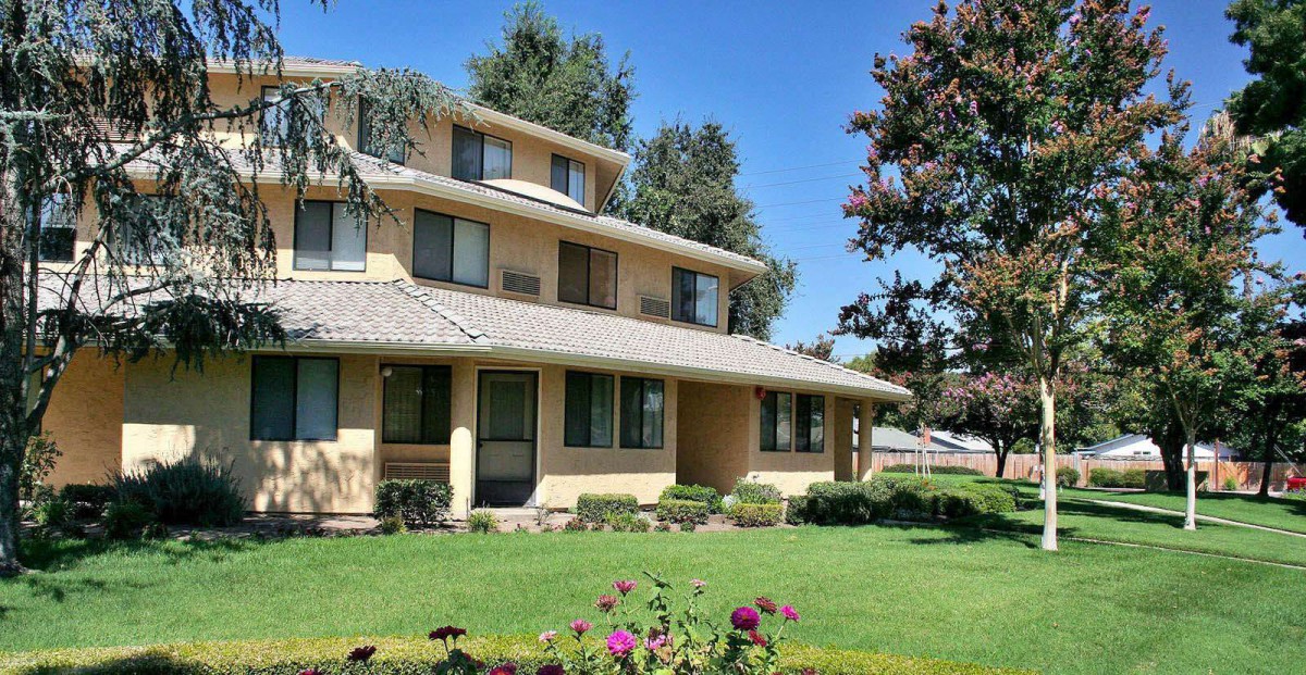 A large suburban house with a well-maintained lawn and trees under a clear blue sky.