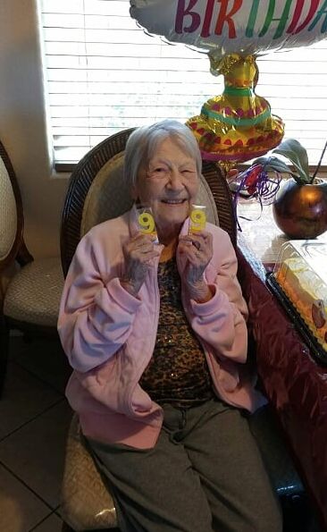 An elderly woman smiling and celebrating her birthday with cake and balloons.