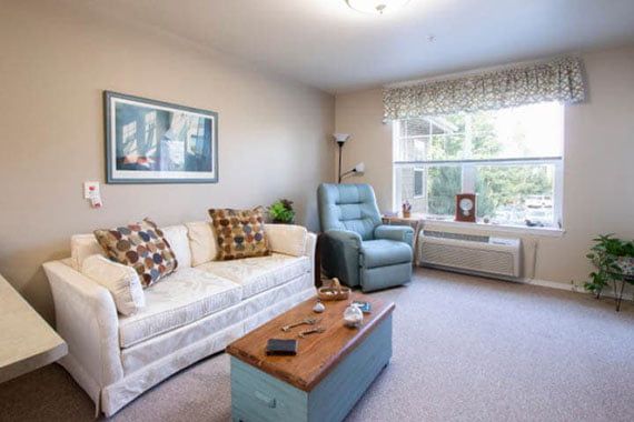 A cozy living room with a sofa, armchair, and coffee table near a large window.