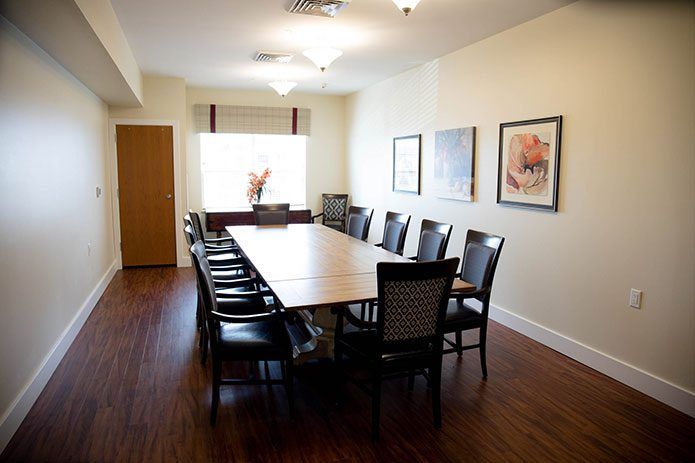 A spacious conference room with a long table and several chairs, featuring artwork on the walls and a wooden floor.