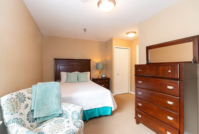 A cozy bedroom with a bed, dresser, and a lamp in a warmly lit room.
