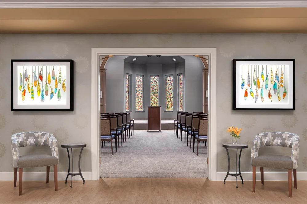 A serene chapel interior featuring rows of chairs, a central podium, and colorful artwork on the walls.