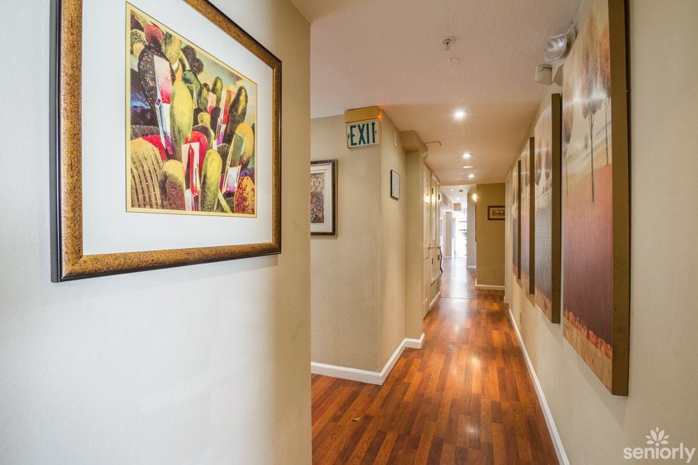 A well-lit hallway featuring artwork on the walls and a wooden floor.