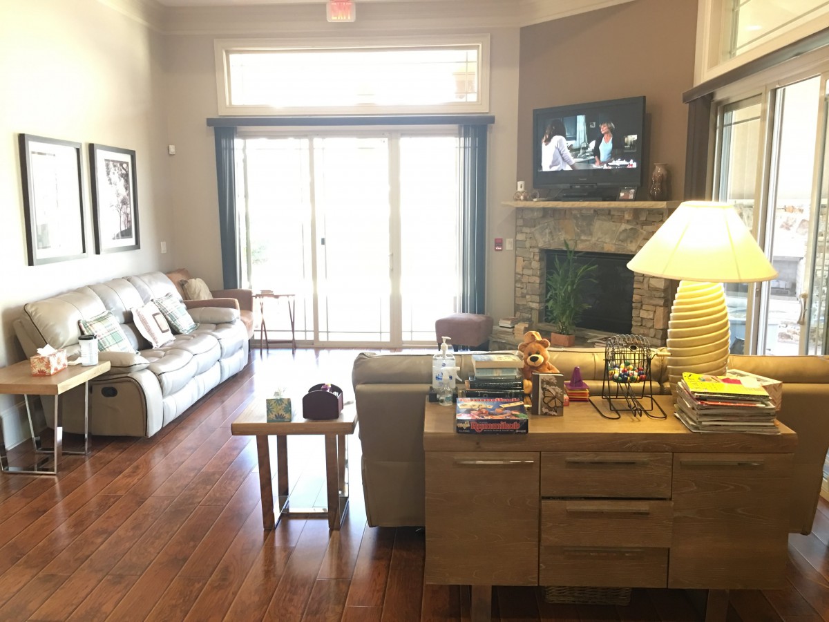 A cozy living room with a sofa, television above the fireplace, and wooden flooring.