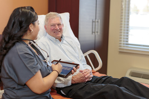 A nurse interacts with an elderly patient while using a tablet in a healthcare setting.