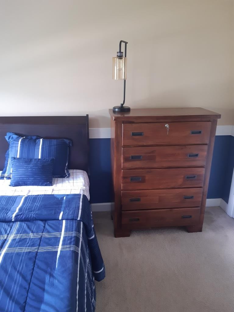 A cozy bedroom featuring a wooden dresser and a bed with blue bedding.