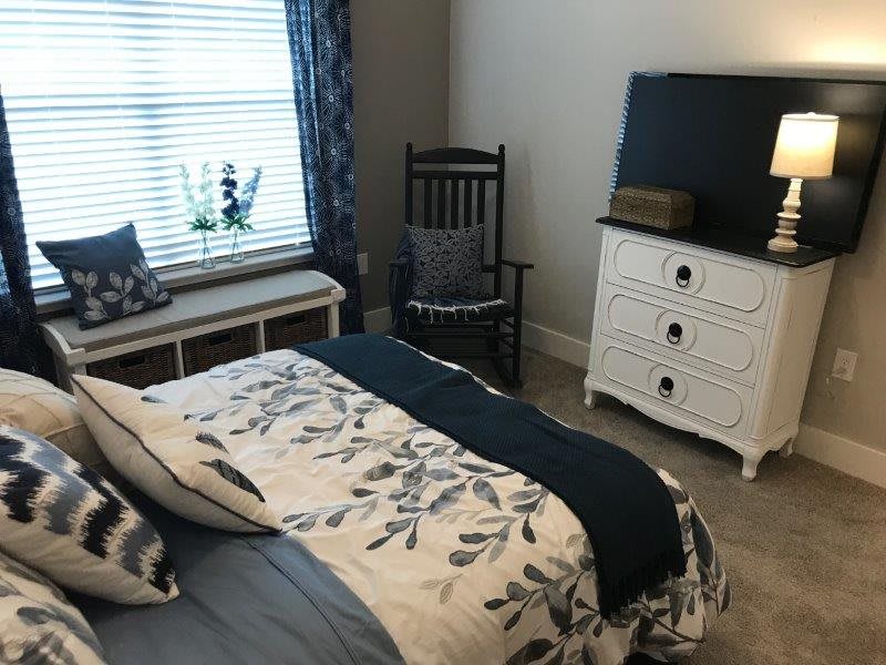 A cozy bedroom with a floral bedspread, a white dresser, and a rocking chair by the window.