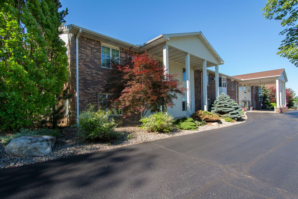 Front view of a residential house with brick exterior, surrounded by landscaped greenery and a paved driveway.