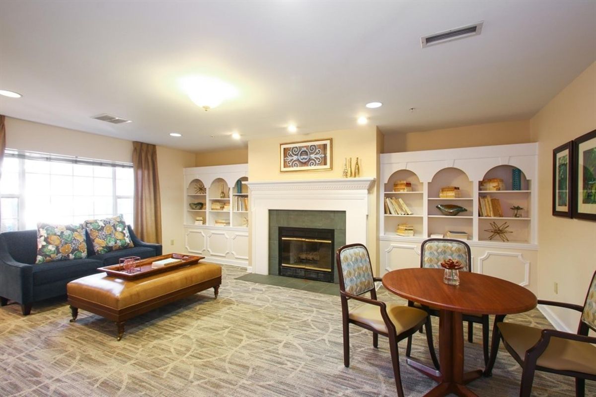 A cozy living room with a fireplace, surrounded by built-in bookshelves, comfortable seating, and a small table and chairs.