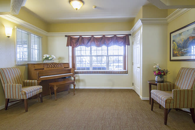 A cozy living room with a piano, chairs, and a large window with curtains.