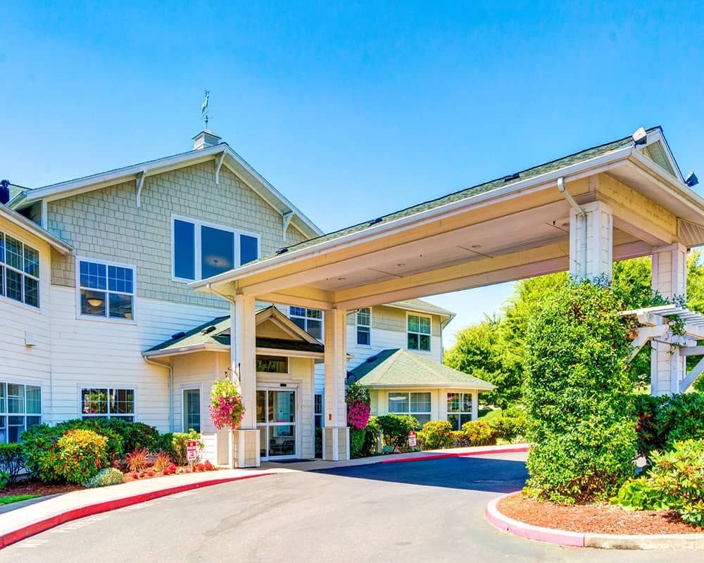 A modern building entrance with an extended awning and landscaped surroundings on a bright, sunny day.