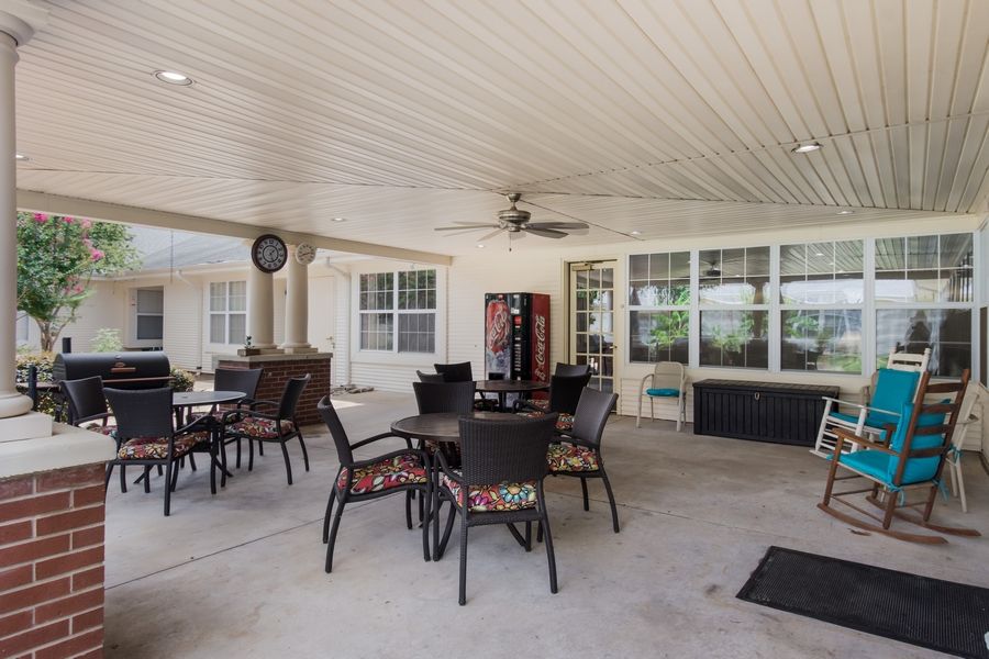 A spacious covered patio with multiple tables, chairs, and a ceiling fan for comfortable outdoor seating.