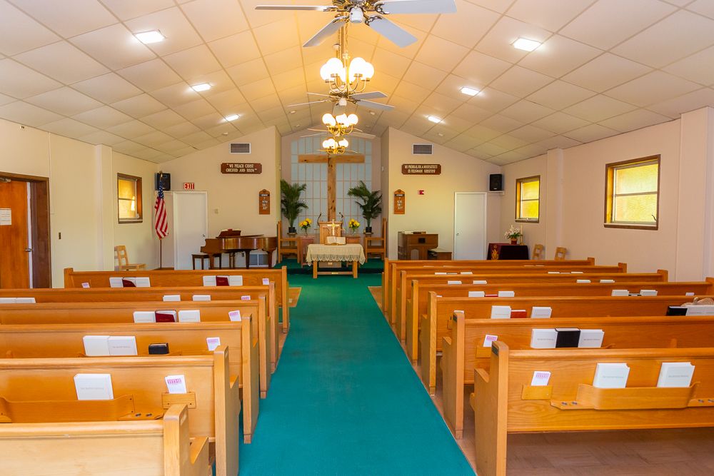 Interior of a church featuring wooden pews, an altar, and a cross at the front.