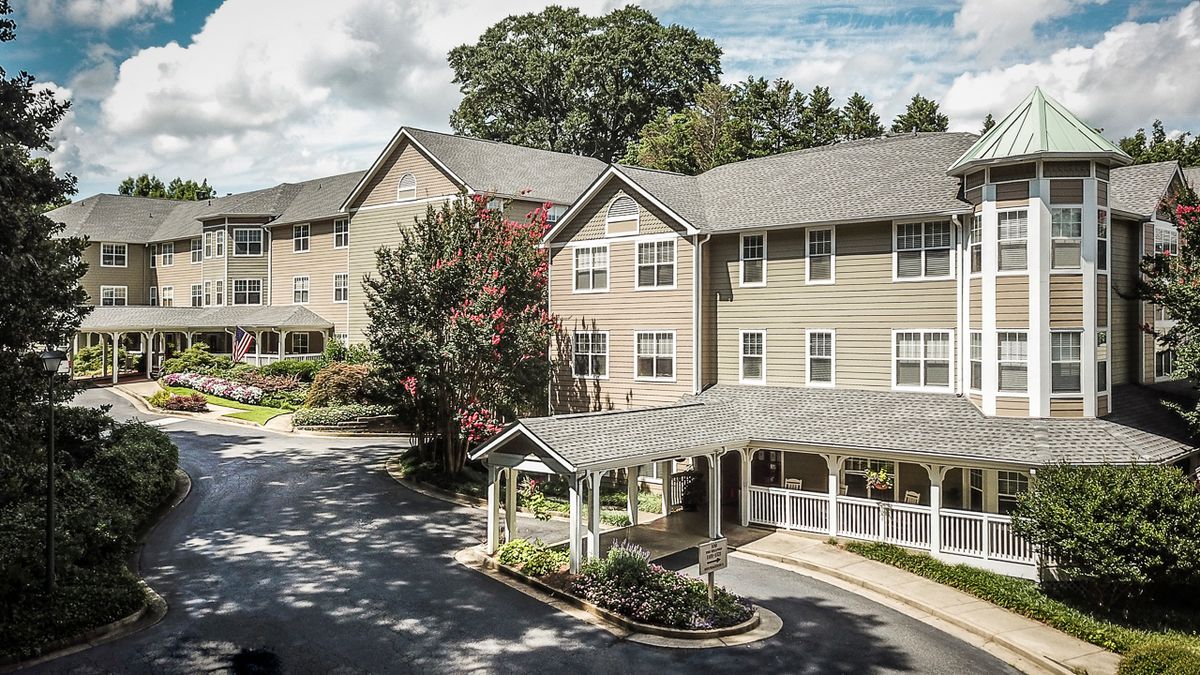 A multi-story residential building surrounded by trees and a small driveway.