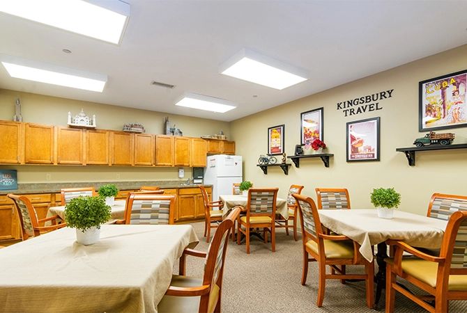 A well-lit dining area with wooden tables and chairs, adorned with plants and decorative artwork on the walls.