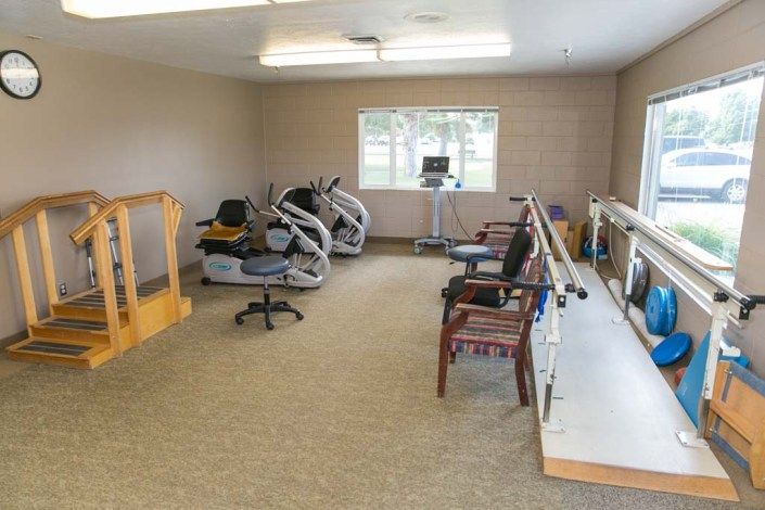 A rehabilitation room equipped with exercise machines, therapy chairs, and parallel bars for physical therapy.