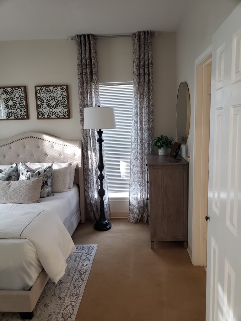 A cozy bedroom with elegant decor, featuring a bed, dresser, and floor lamp.