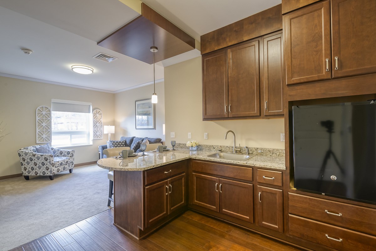 A modern open floor plan kitchen with wooden cabinets and granite countertops, adjacent to a cozy living room.