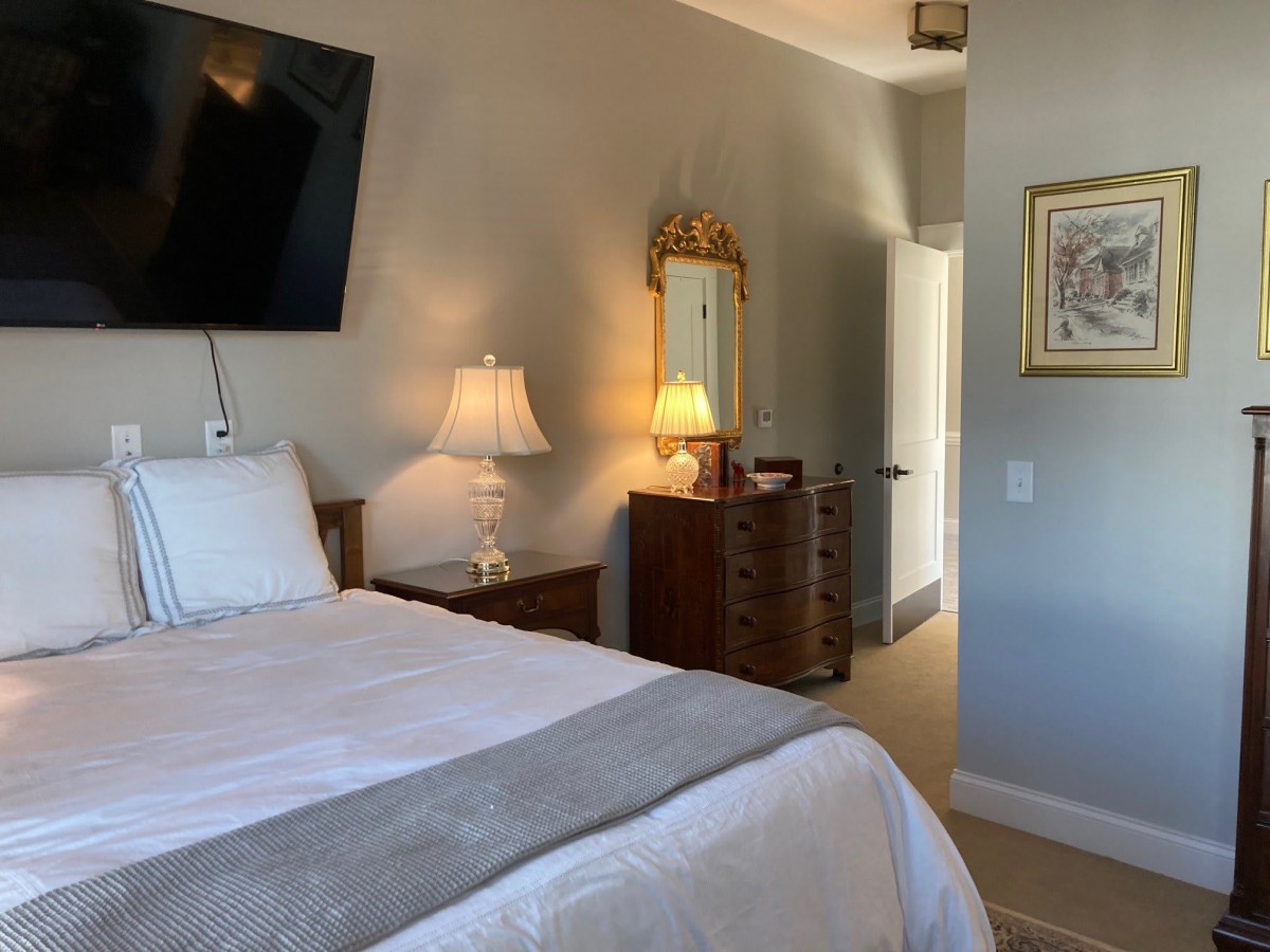 A cozy bedroom with a neatly made bed, wall-mounted television, and warm lighting from bedside lamps.