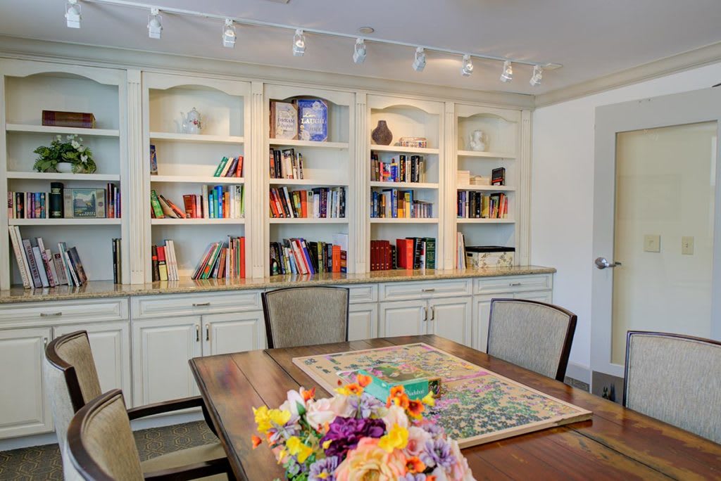 A cozy dining room featuring a wooden table with vibrant flowers and a large bookshelf filled with various books.