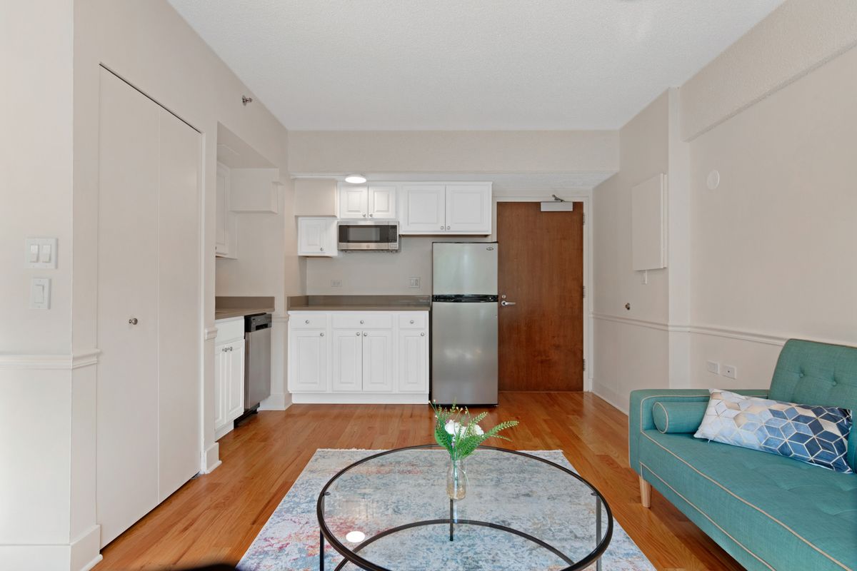 A modern apartment interior featuring a compact kitchen and living area with sleek furniture and wooden flooring.