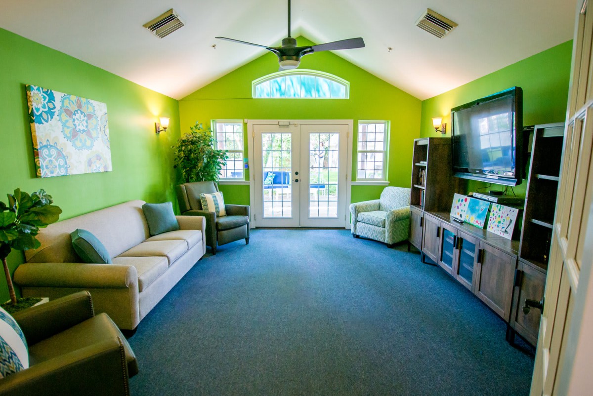 A bright and colorful living room with green walls, featuring comfortable seating and a television.
