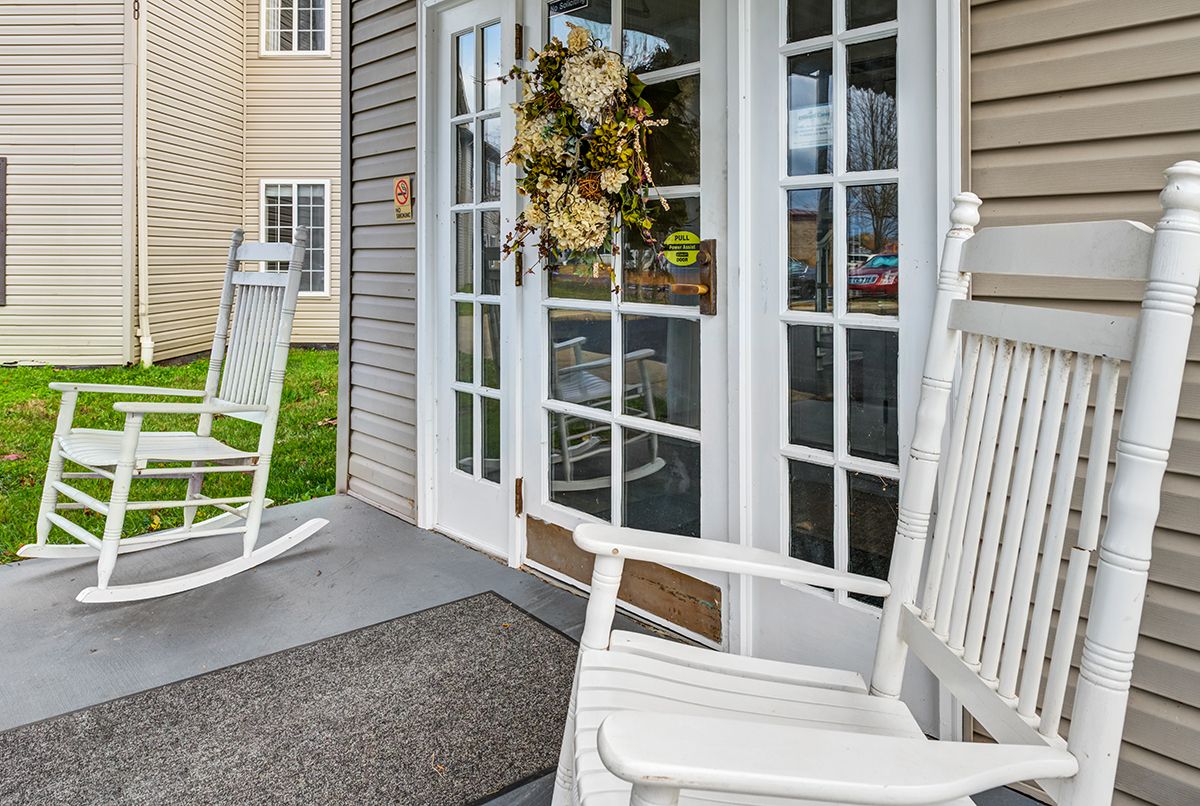 A cozy porch with white rocking chairs and a decorative wreath on the door.