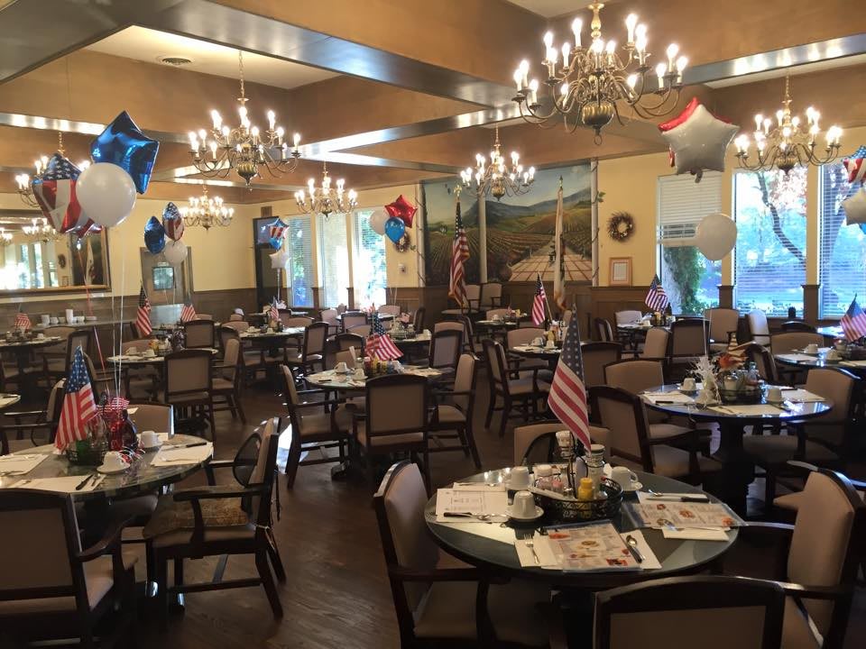 A decorated dining area with balloons and flags, featuring multiple tables and elegant chandeliers.