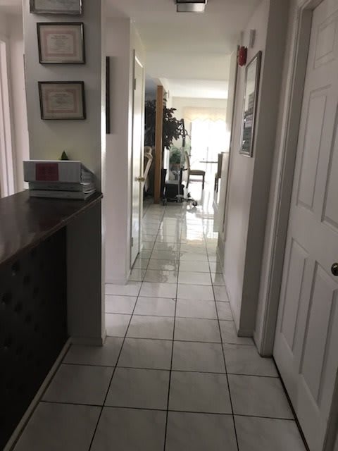 A view down a tiled hallway in a home, leading to a bright room with furniture and decor.